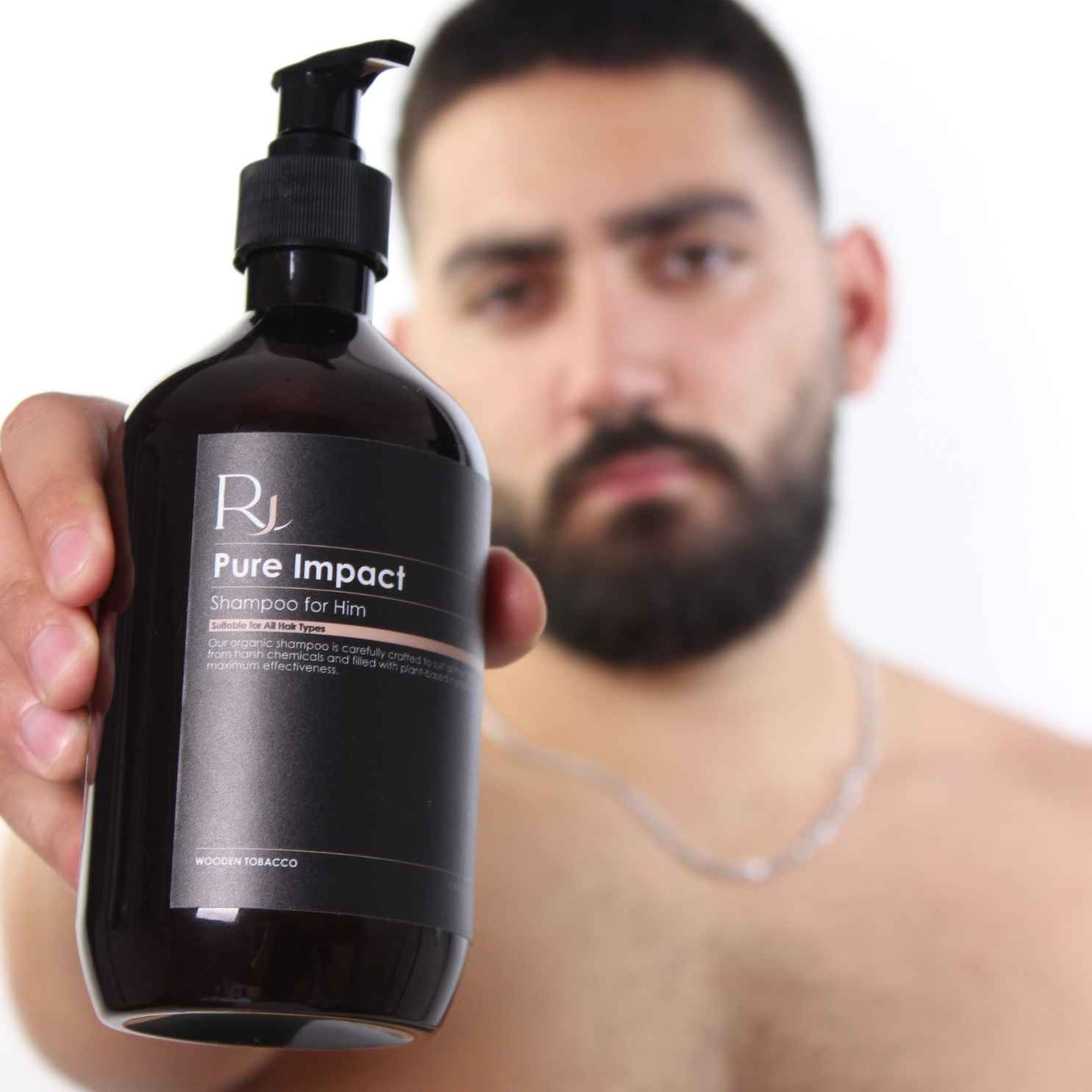 Bottle of Raqiia Pure Impact Shampoo for men held by a person with a blurred background