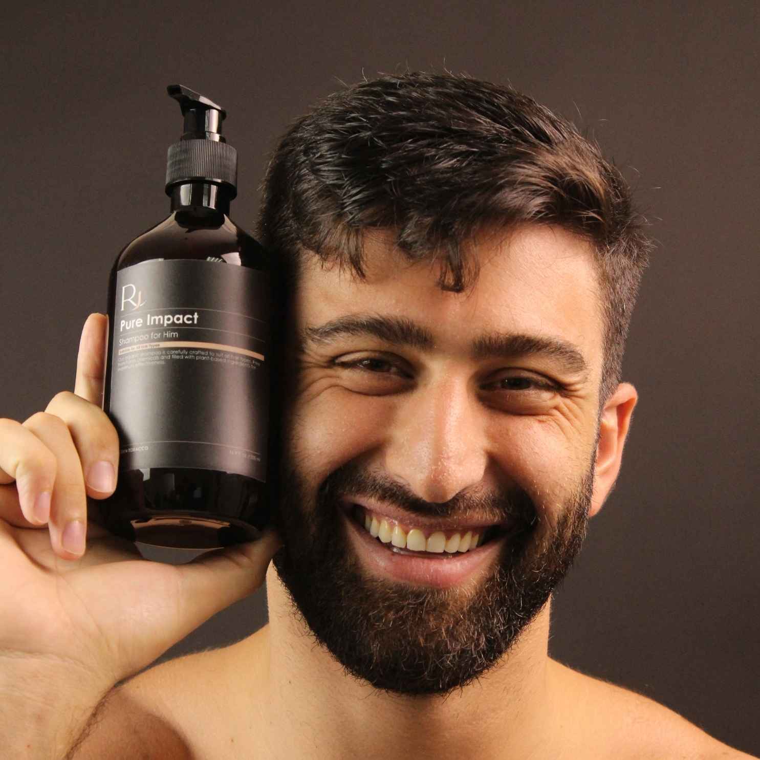 Man holding a bottle of Raqiia Pure Impact Shampoo against a dark background