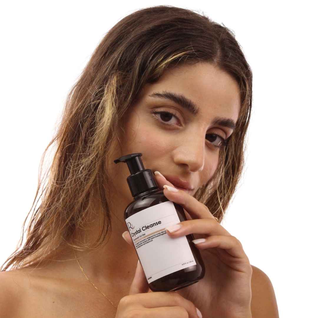 Woman holding a bottle of 'Raqiia Crystal Cleanse Facewash' on a white background