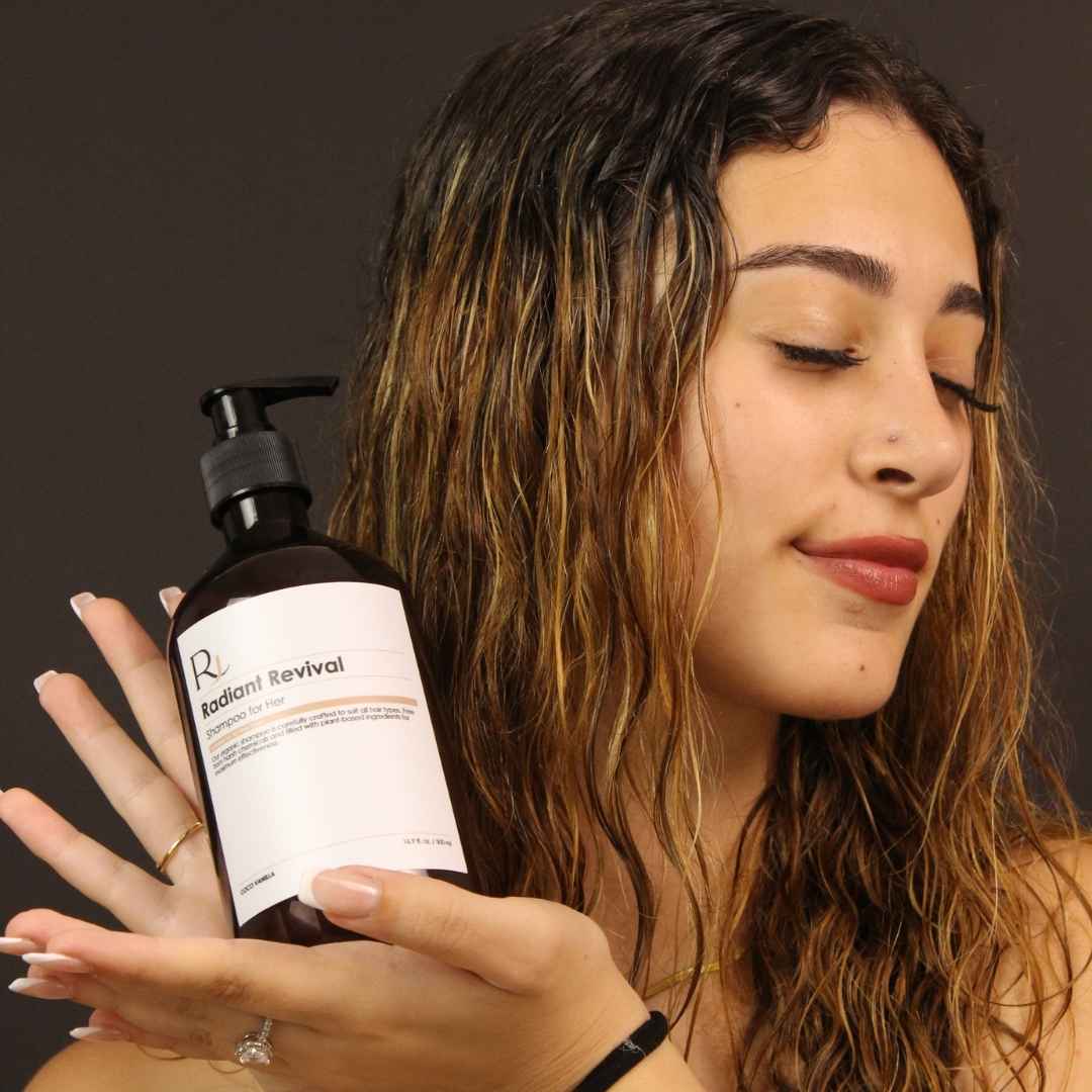 Woman holding a bottle of Raqiia Radiant Revival shampoo with a dark background