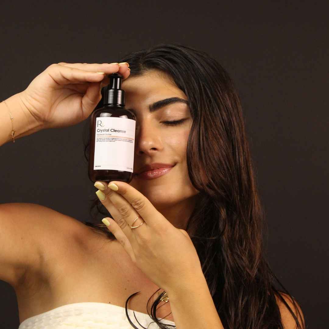 Woman holding a bottle of 'Raqiia Crystal Cleanser Facewash' against a dark background