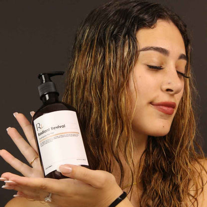 Woman holding a bottle of Raqiia Radiant Revival shampoo with a dark background
